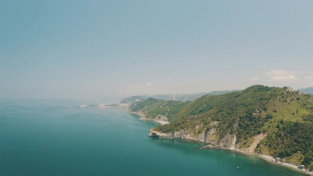 Drone view of the lighthouse in the trees, the white lighthouse building built on the edge of the cliff