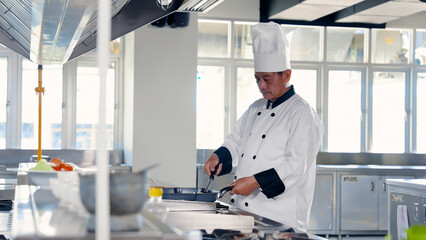 Naklejka premium Chef holding a golden ladle in a frying pan in the kitchen Prepare food for teaching students in cooking class. Learn to cook Thai food. on campus