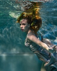 portrait of a fashionable girl underwater in a pool in a long dress