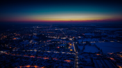 Fototapeta na wymiar Flight over a city illuminated by a sunset flare. City lantern lights from above. A small town from above. Selective soft focus