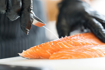 Chef preparing a fresh salmon fillet in Japanese kitchen. Close up hand of chef Pulling salmon fish bone for making sashimi.