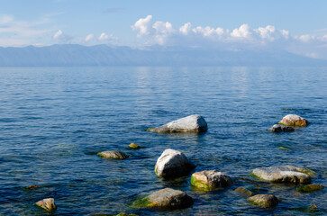 The smooth surface of the water of Lake Baikal on a sunny summer day. Large stones in the water near the shore.