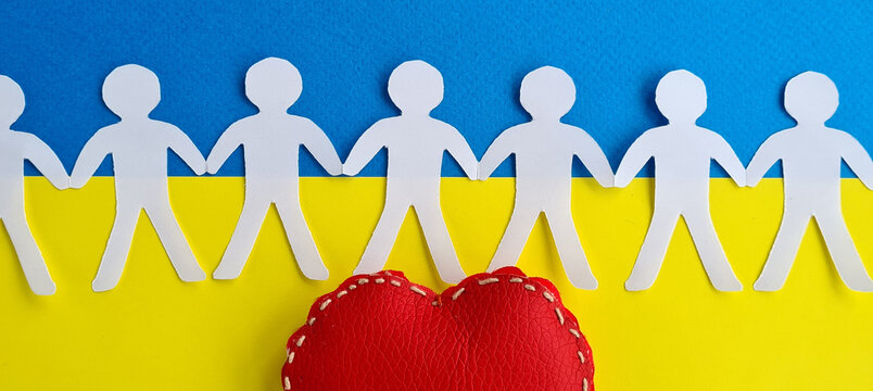 Figures of paper people hold hands against background of Ukrainian flag and red heart