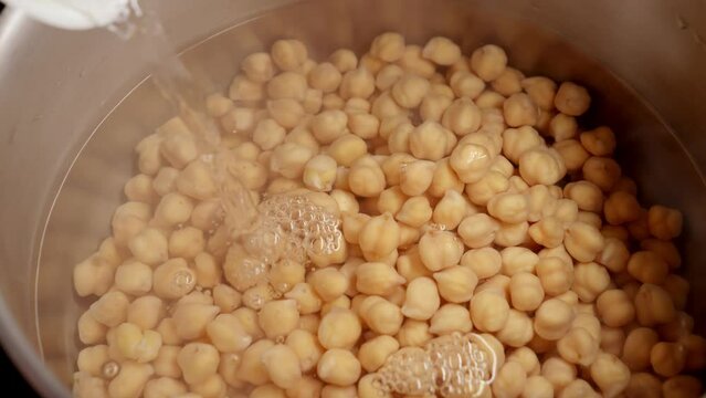 Slow motion of pouring boiling water in pan with cooking chickpeas. Cooking legume, healthy nutrition, vegan food.