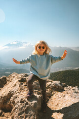 Child traveler hiking in mountains raised hands travel family healthy lifestyle active summer vacations outdoor smiling girl 4 years old - 575541616