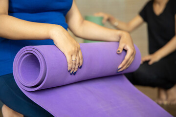Closeup of young indian woman rolling her purple color yoga mat after finishing her class or fitness lesson.