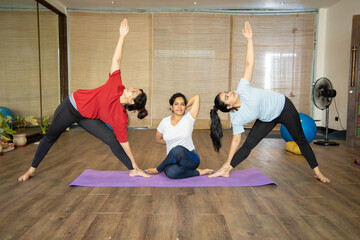 Three young indian women practicing yoga asana together at indoor studio.