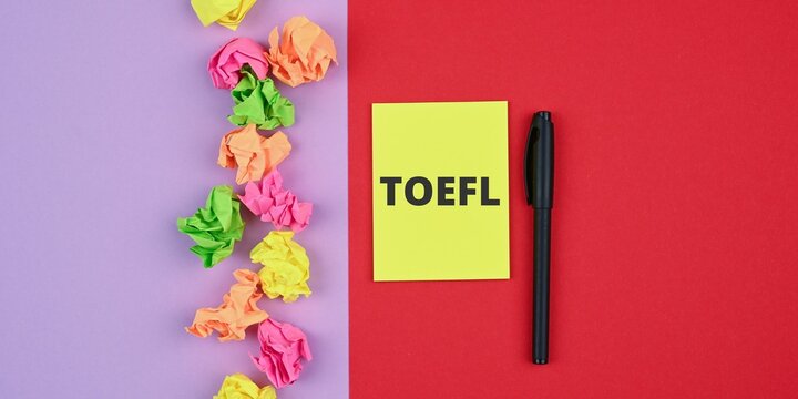 TOEFL word on yellow sticky note paper. Pen and sticky notes on a red-violet surface. 