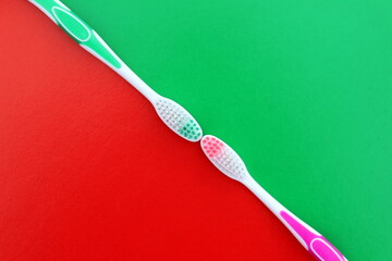 Two toothbrushes of different colors lie on a red and green background.	