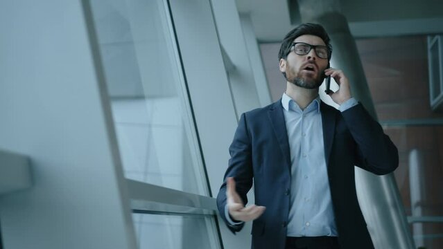 Close-up of a stressed entrepreneur wearing glasses. Portrait of annoyed guy in formal suit having emotional telephone call in modern office. High quality 4k footage