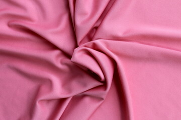 Thin bright knitted fabric lies twisted, top view.