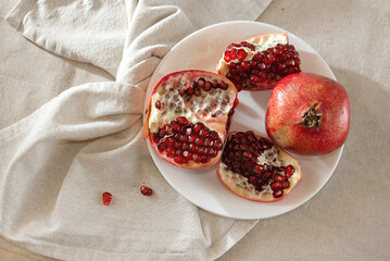 Red ripe pomegranates on plate on beige tablecloth, copy space. Aesthetic lifestyle composition...