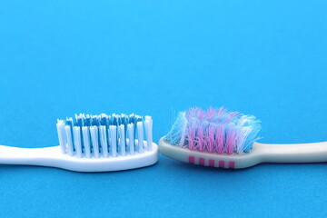 On a blue background are two toothbrushes, one old, used and the other new.