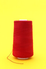  On a yellow background is a large spool of red thread.