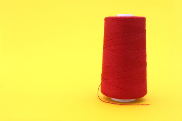 On a yellow background is a large spool of red thread.