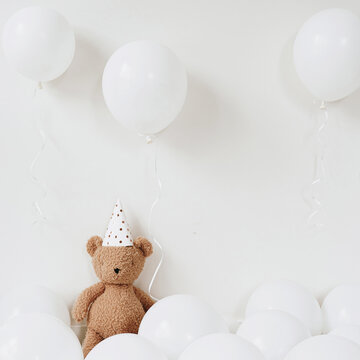 Naklejka Teddy bear in party hat sitting near balloons over white background