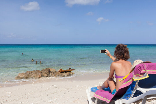 A girl 20 30 years old sunbathing on a beautiful beach in Cuba with her smartphone in the hands