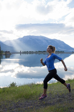 Young woman runs along edge of mtn lake, sunrise