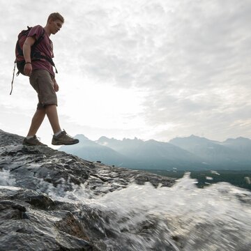 Young man hikes down ridge past mtn stream