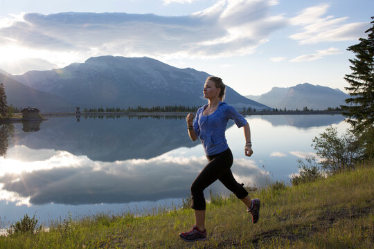 Young woman runs along edge of mtn lake, sunrise