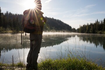 Hiker pauses at edge of mountain lake, sunrise