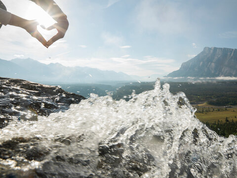 Hands form heart shape above mountain creek