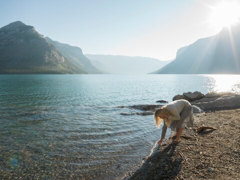 Woman beachcombs along edge of mountain lake