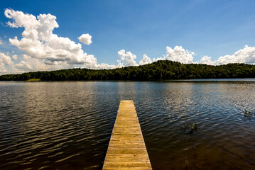 Small dock jutting into calm lake with hills and clouds in distance