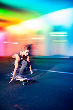 Young man skateboarding in colorfully lit traffic tunnel