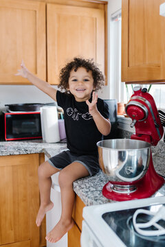 Excited celebrating biracial toddler baking and sitting on counter