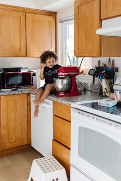 Biracial boy toddler sitting on kitchen counter baking cookies