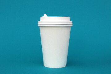  A bright disposable paper cup for coffee stands on a turquoise background.