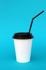 A bright disposable paper cup for coffee stands on a turquoise background.