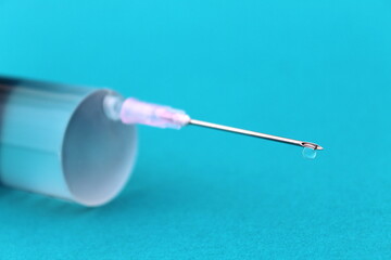 A large syringe with a sharp needle lies on a turquoise background.