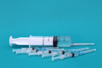 On a turquoise background, there are many small syringes with a vaccine and one large one.