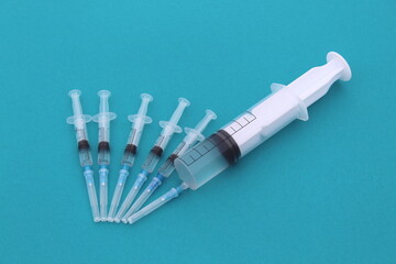  On a turquoise background, there are many small syringes with a vaccine and one large one.