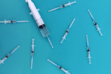  On a turquoise background, there are many small syringes with a vaccine and one large one.