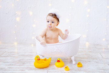 a joyful baby girl of six months is bathing in a bath with foam and rubber ducks, a small child is...