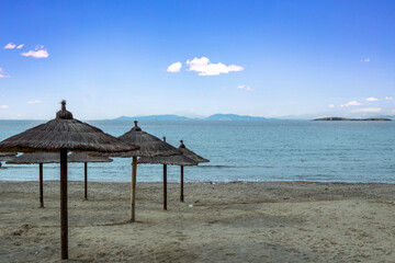 Straw parasol on empty sandy beach. Sea, blue sky background. Polluted seaside with plastic bottle.