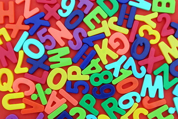 Background of bright multi-colored plastic letters lying on a red background.	