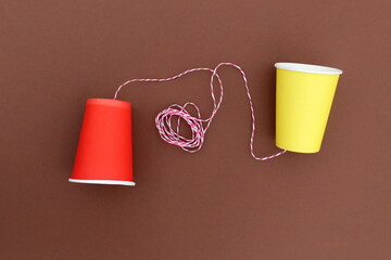 An impromptu telephone made of bright paper glasses with a rope on a brown background.