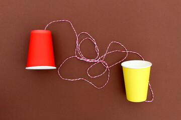 An impromptu telephone made of bright paper glasses with a rope on a brown background.