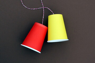 An impromptu telephone made of bright paper glasses with a rope on a brown background.