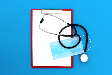 On a blue background lies a tablet with blank paper and a stethoscope. View from above.