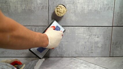 The master rubs the tile with a spatula. Repair and wall tiling. The master rubs the seams of the...