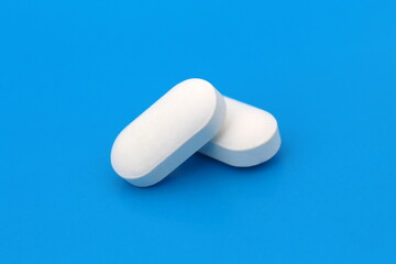 Two white pills lie on a blue background.
