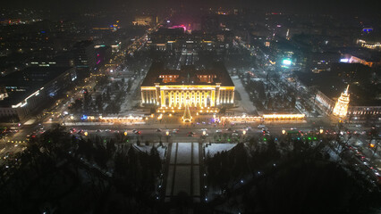 Fototapeta na wymiar A large Christmas tree in the lights on the square. Top view from the drone on the street with cars and people, a bright building in garlands, various decorations for the new year. Almaty, December