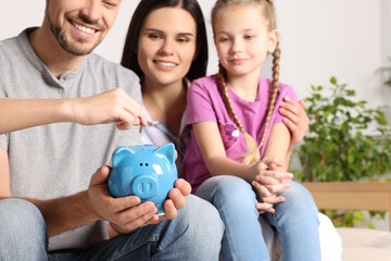 Happy family putting coin into piggy bank at home, closeup