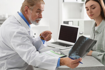 Fototapeta na wymiar Orthopedist showing X-ray picture to patient in clinic