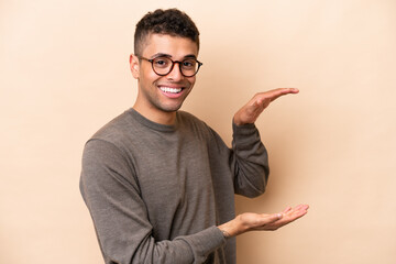 Young Brazilian man isolated on beige background holding copyspace to insert an ad